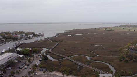 Aerial-rising-dolly-shot-of-the-Shem-Creek-boardwalk-along-Charleston-Harbor-on-a-hazy-day-in-Mount-Pleasant,-South-Carolina