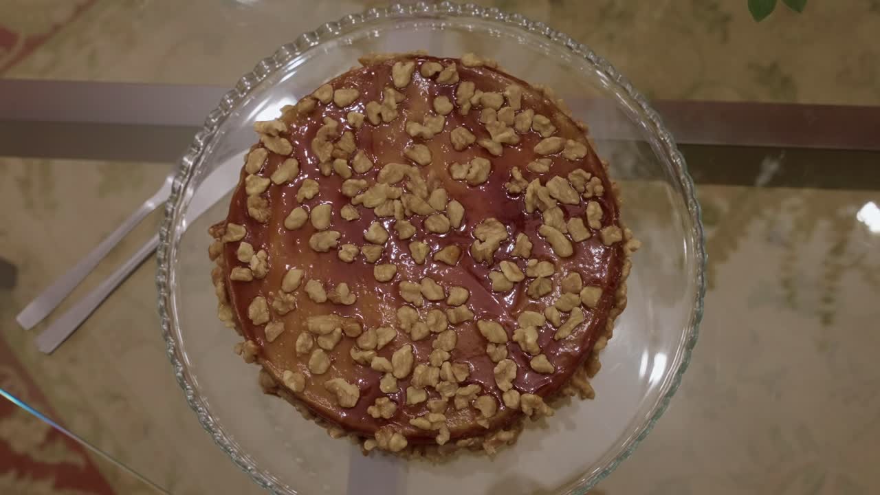 Top view of a caramel cake topped with chopped walnuts placed on a clear glass plate