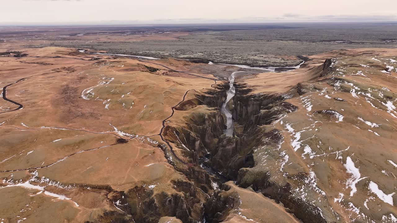Breathtaking aerial of Iceland’s Fjaðrárgljúfur Canyon with winding river, volcanic hills and patches of melting snow.