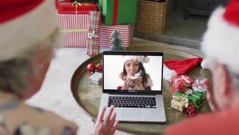 Senior-caucasian-couple-with-santa-hats-using-laptop-for-christmas-video-call-with-woman-on-screen