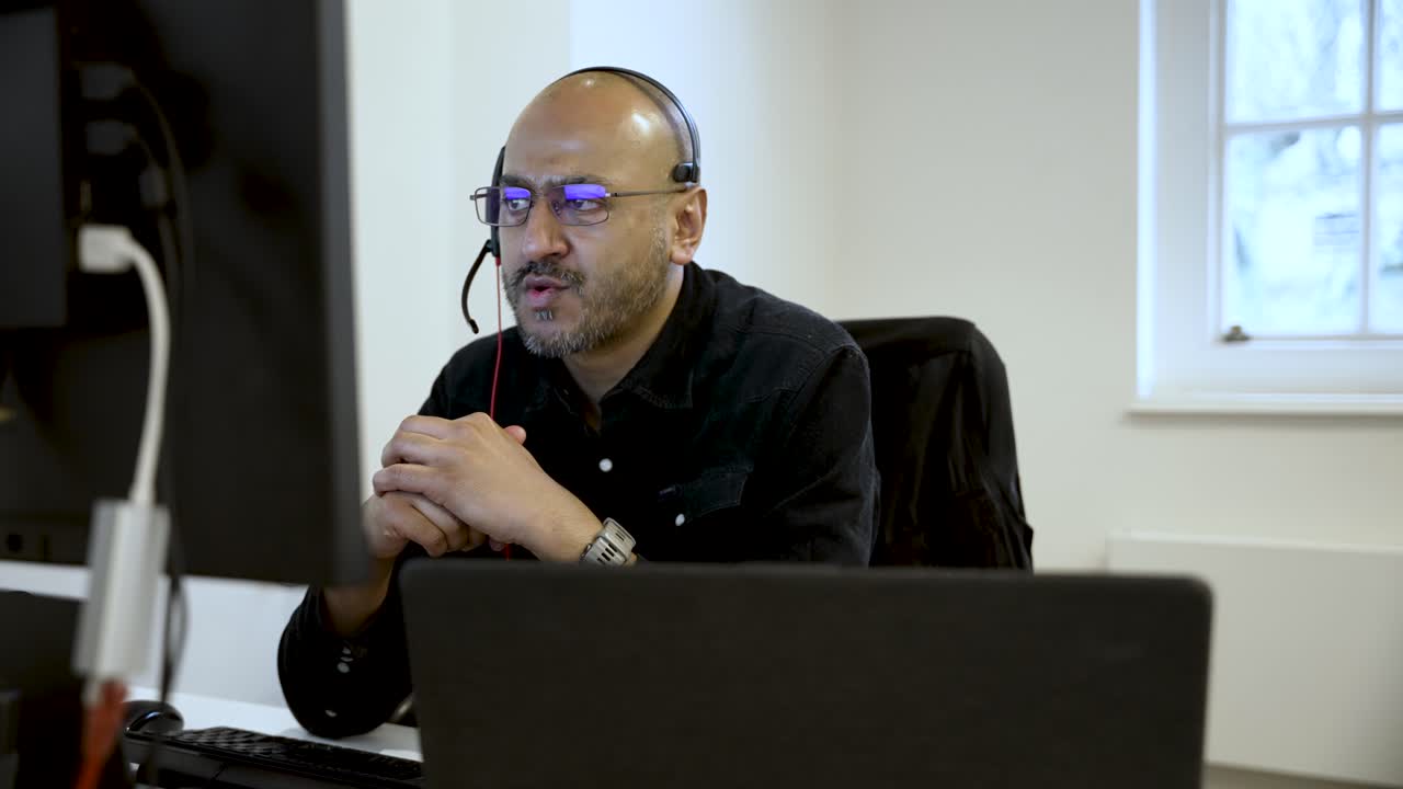 Businessman working from a home office, wearing a headset while engaging with the computer screen and managing online tasks