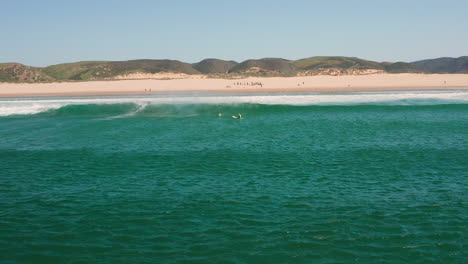 Aerial:-Surfing-the-beach-of-Bordeira-in-the-Algarve,-Portugal