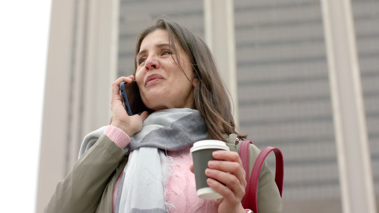 Donna anziana che risponde a una telefonata sul marciapiede, ride e parla mentre tiene una tazza di caffè
