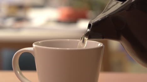 close-up shot, pouring hot tea from a black teapot into a white cup