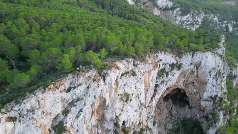 Wanderer-Ruhen-Sich-Auf-Einer-Felsklippe-Zwischen-Bäumen-Aus-Und-Haben-Bei-Sonnenuntergang-Auf-Ibiza-Blick-Auf-Die-Grüne-Landschaft