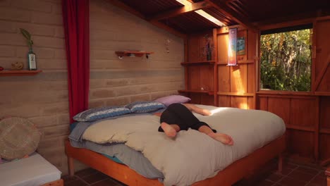 young woman happily jumps on bed in rented private cabin in lake atitlan, guatemala, central america