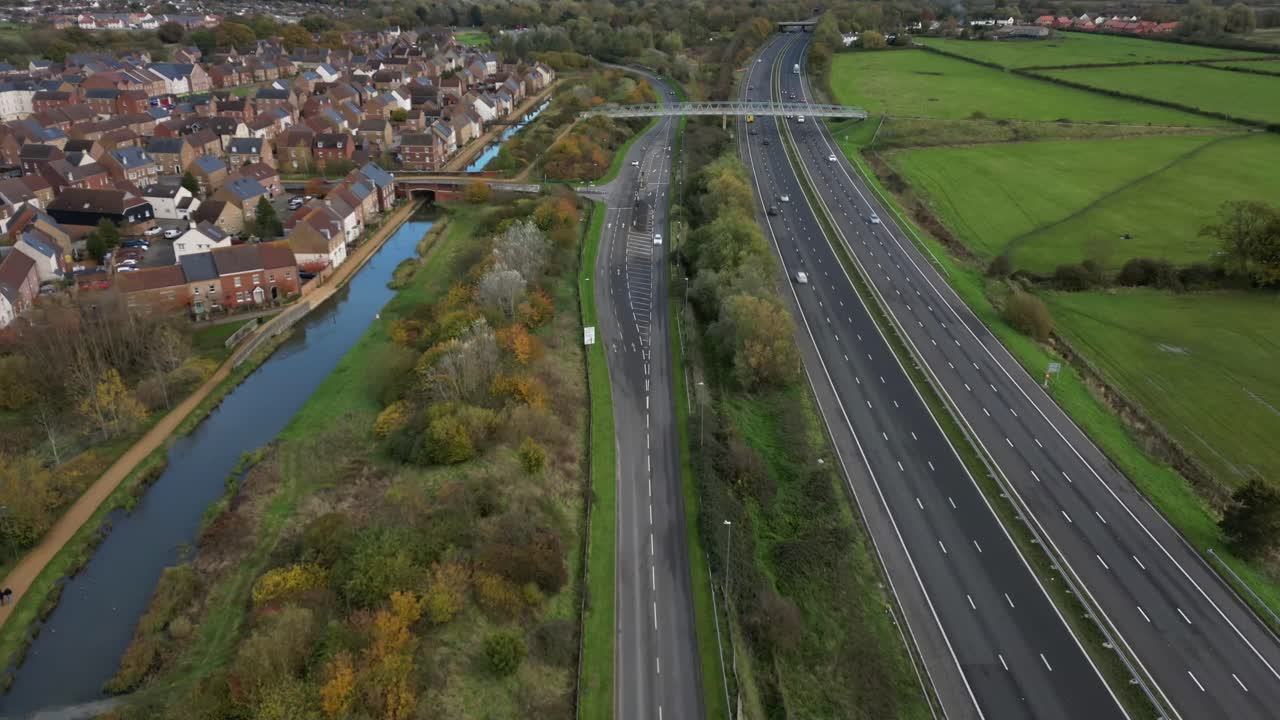 Dynamic drone video of M271 highway stretching through Southampton near Redbridge. Captures movement of vehicles, suburban homes, lush greenery, and autumn colors from above. Crisp, clear visual