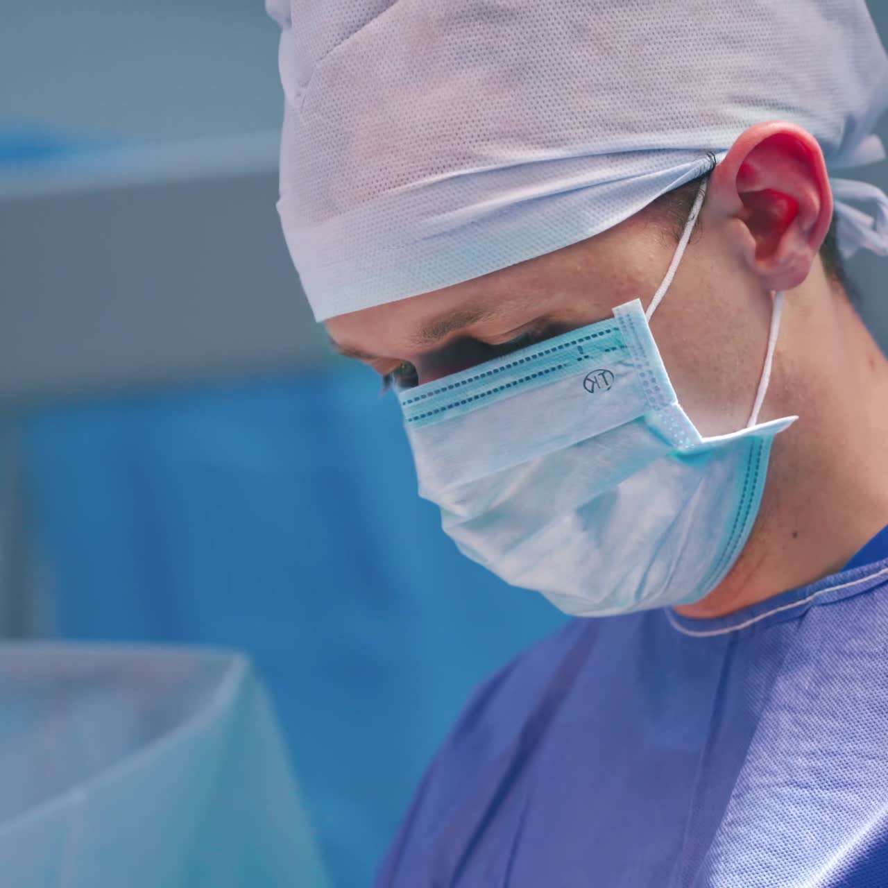 Portrait of young surgeon in blue mask. Face of a specialist in medical uniform looking down during operation. Close-up.