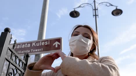 hermosa chica con máscara médica protectora y ropa de moda muestra el signo de la torre de galata nuevo estilo de vida normal, concepto de viaje