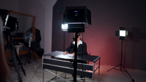 female reporter in black jacket sits in the photo studio. silhouette of a lady standing backstage.