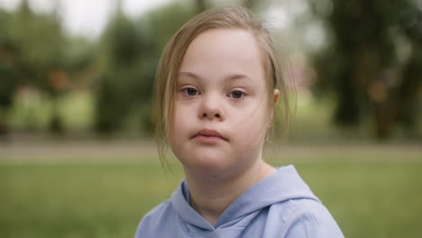 close-up view of a little girl with down syndrome looking at camera sitting on the grass in the park