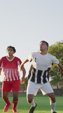 video vertical de dos jugadores de fútbol diversos en el campo pateando la pelota