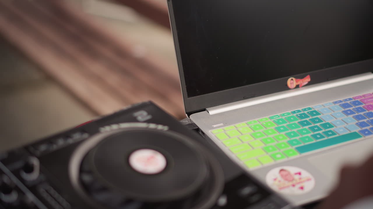 dj laptop and controller closeup, focused preparation by producer adjusting decks, colorful key cover on laptop, closeup hands tweaking tempo and loop, rainspeckled table, urban bench background