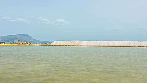 Zeitraffer-Vor-Der-Italienischen-Küste-Siziliens-In-Torre-Nubia-Mit-Blick-Auf-Das-Ruhige,-Spiegelnde-Meer-Mit-Gebäuden-Und-Den-Bergen-Im-Hintergrund-An-Einem-Sonnigen-Sommertag