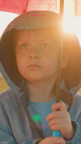 offended boy beneath umbrella shelter. child sadness seems to blend with rain becoming indistinguishable from tears of sky. inner turmoil during solitary walk