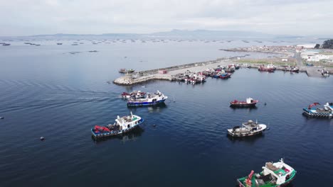 Aerial-drone-shot-of-beautiful-fishing-motor-port-along-with-yachts-docked-on-a-cloudy-day-with-the-view-of-mountain-range-in-the-background