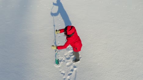 a woman struggles as she drilled hole for fishing on frozen lake using manual auger during sunny winter day