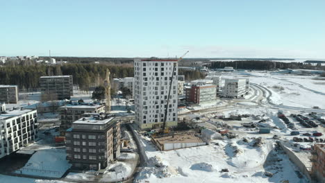 Antenne,-Drohnenschuss,-In-Richtung-Einer-Baustelle,-Kräne,-Die-Ein-Mehrfamilienhaus-Bauen,-An-Einem-Sonnigen-Wintertag,-Bei-Pielisjoki-In-Joensuu,-Pohjois-Karjala,-Finnland