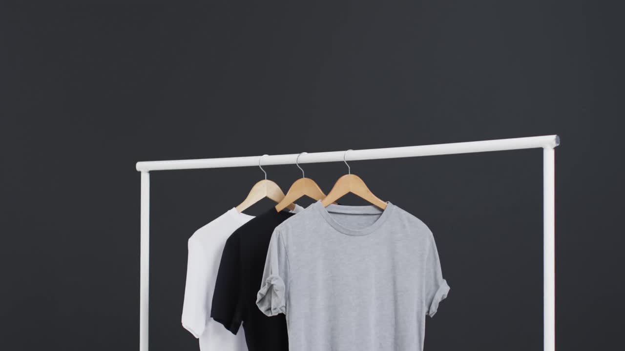Video of three white, black and grey t shirts on hangers and copy space on black background