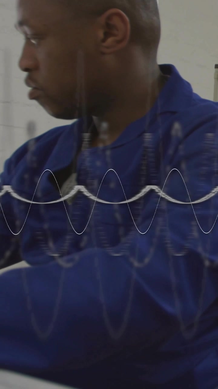 Video verticale: Tecnico che scansiona uno strumento fuori campo, girando la testa mentre una forma d'onda traccia un segnale in un'officina.