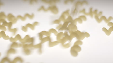 Dried-yellow-cavatappi-pasta-falling-into-frame-onto-a-backlit-suface-in-slow-motion