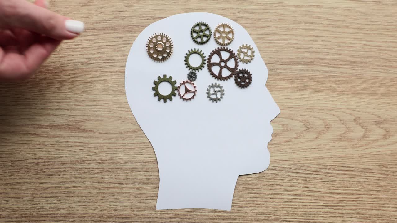 A hand placing gears into a human head cutout, symbolizing thinking and intelligence