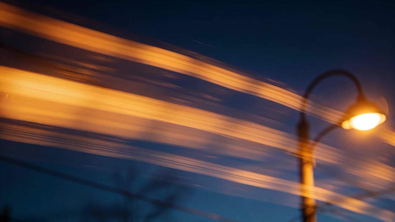 Standing ornate streetlamp glowing on dusk street passing cars creating orange trails, copy space