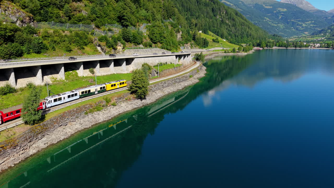 Scenic train by Swiss lake, clear sky reflecting in water, serene view