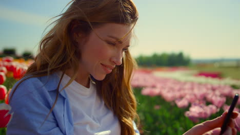 young lady sending kisses online via mobile phone while walk in flower park.