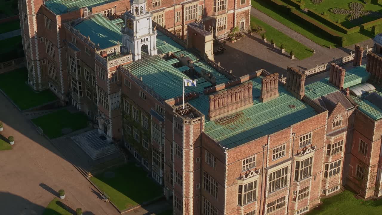 Aerial view circling above Hatfield house corner rooftop with flag blowing in the breeze