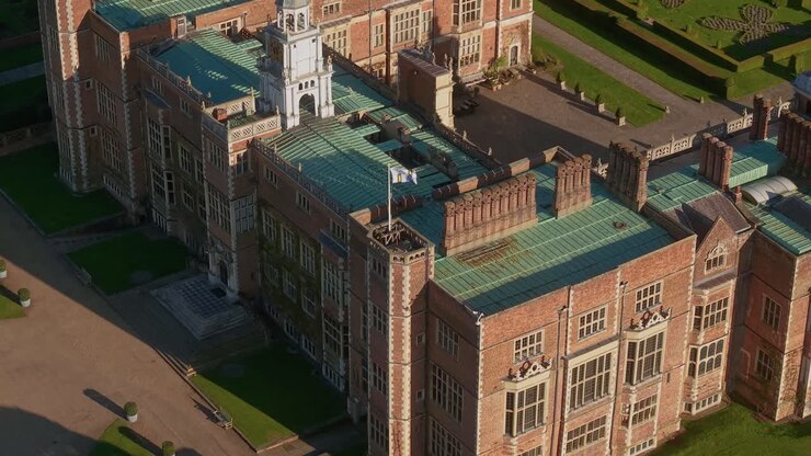 Aerial view circling above Hatfield house corner rooftop with flag blowing in the breeze