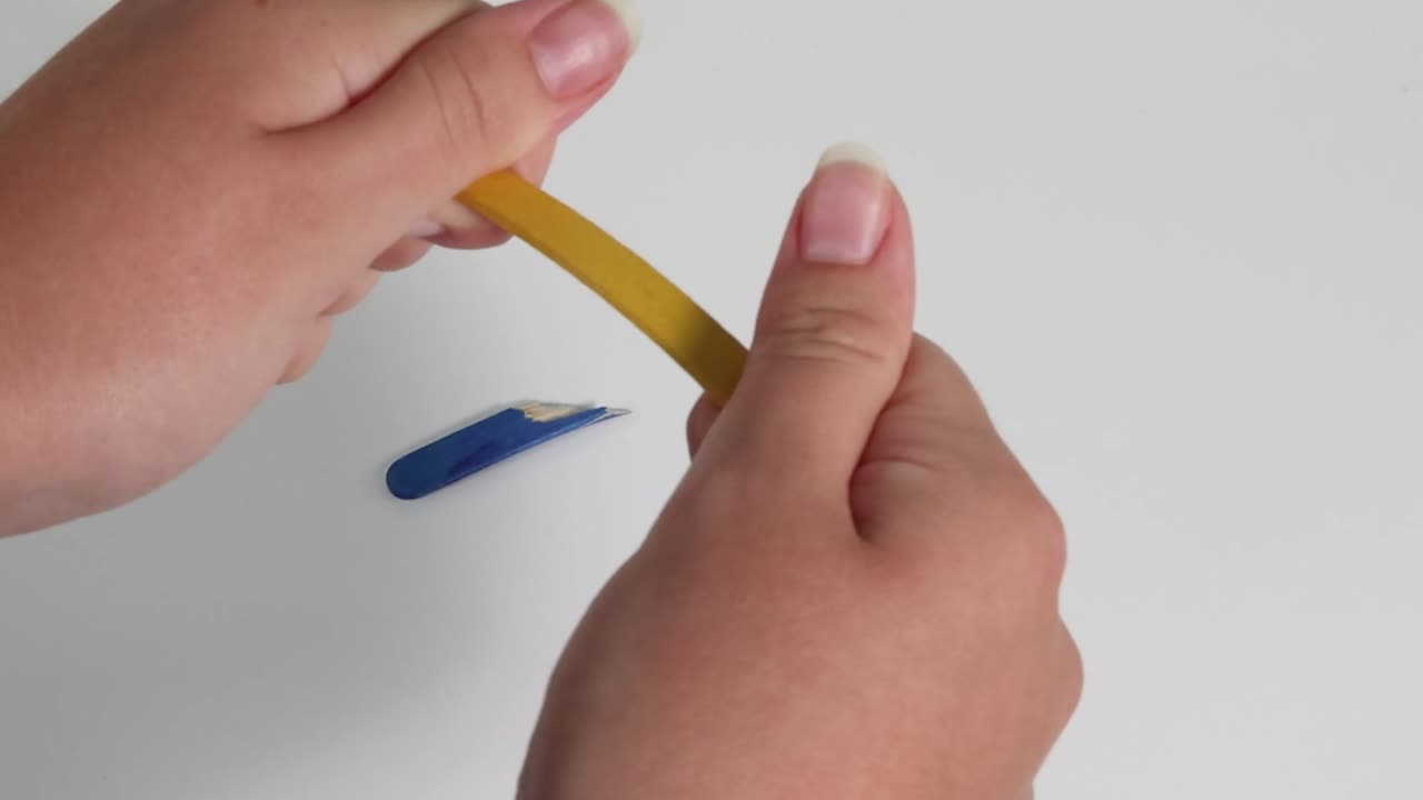 Primo piano di mani che piegano una matita gialla, con trucioli di matita blu visibili su una superficie bianca