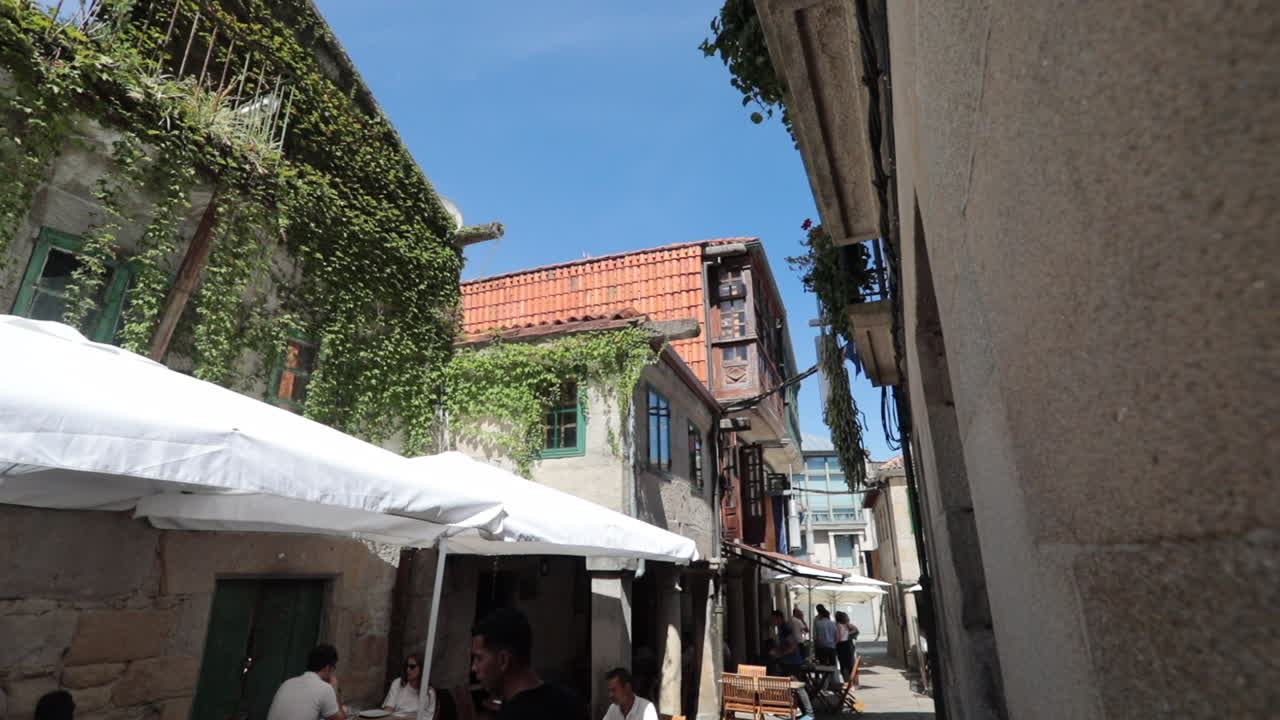 Narrow street with old stone buildings and green ivy in Pontevedra, Galicia, under a clear sky