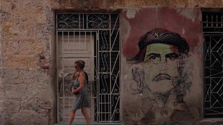 People walking past a Che Guevara mural on a street wall