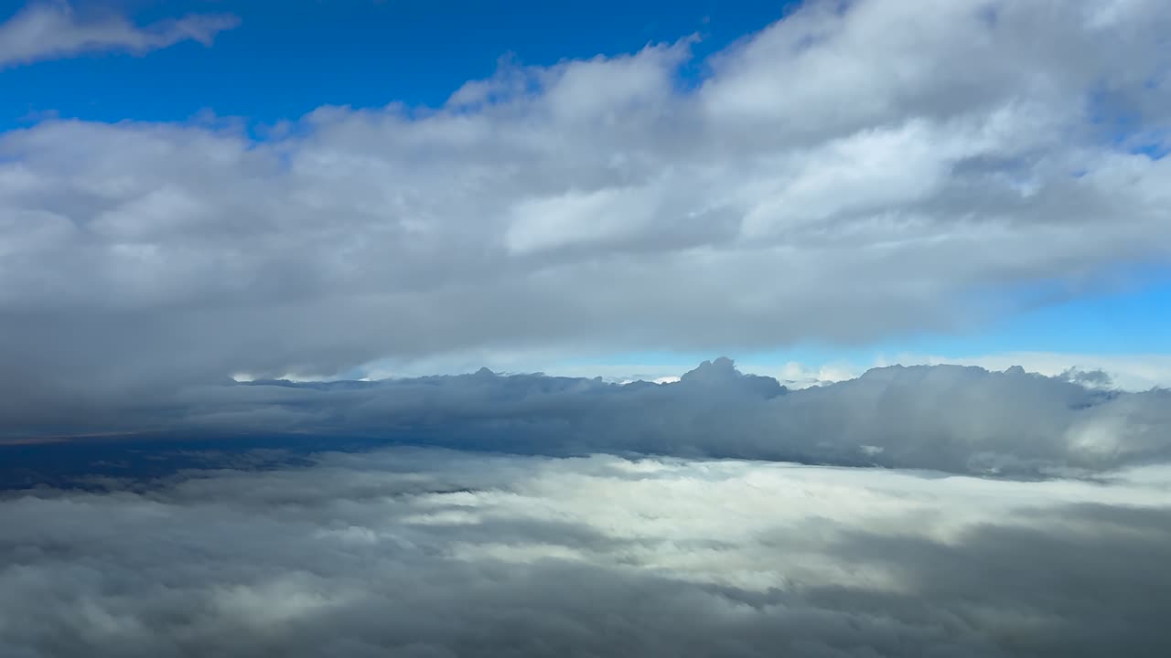 Aerial view through the pilot’s eye while flying peacefully between endless layers of stratus clouds in a blue sky, captured from a jet cockpit