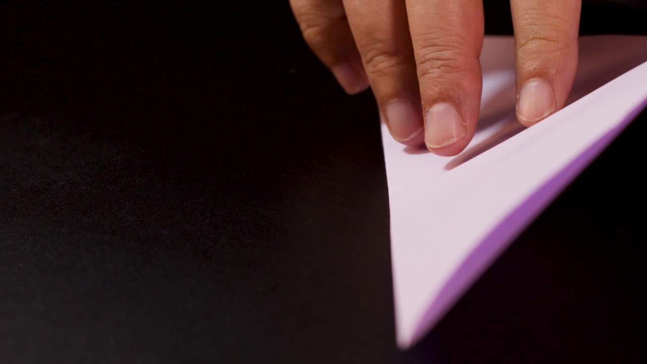 Close-up hands folding pastel paper into origami boat, studio lighting, steady camera, dark background