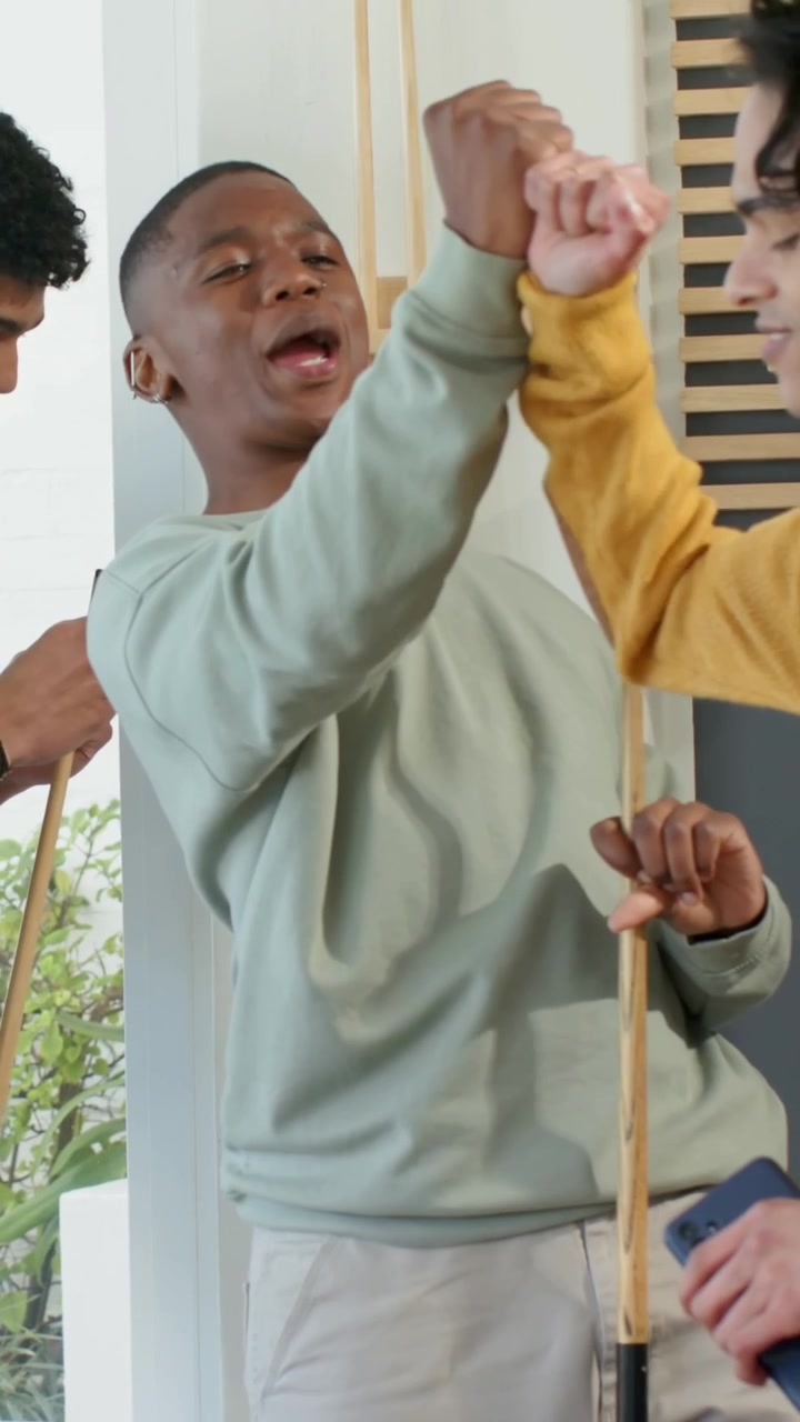 Vertical video: Smiling man in green sweater holding cue as friend adjusting cue home playing pool
