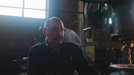 labourer with spectacles sits by drilling machine at factory