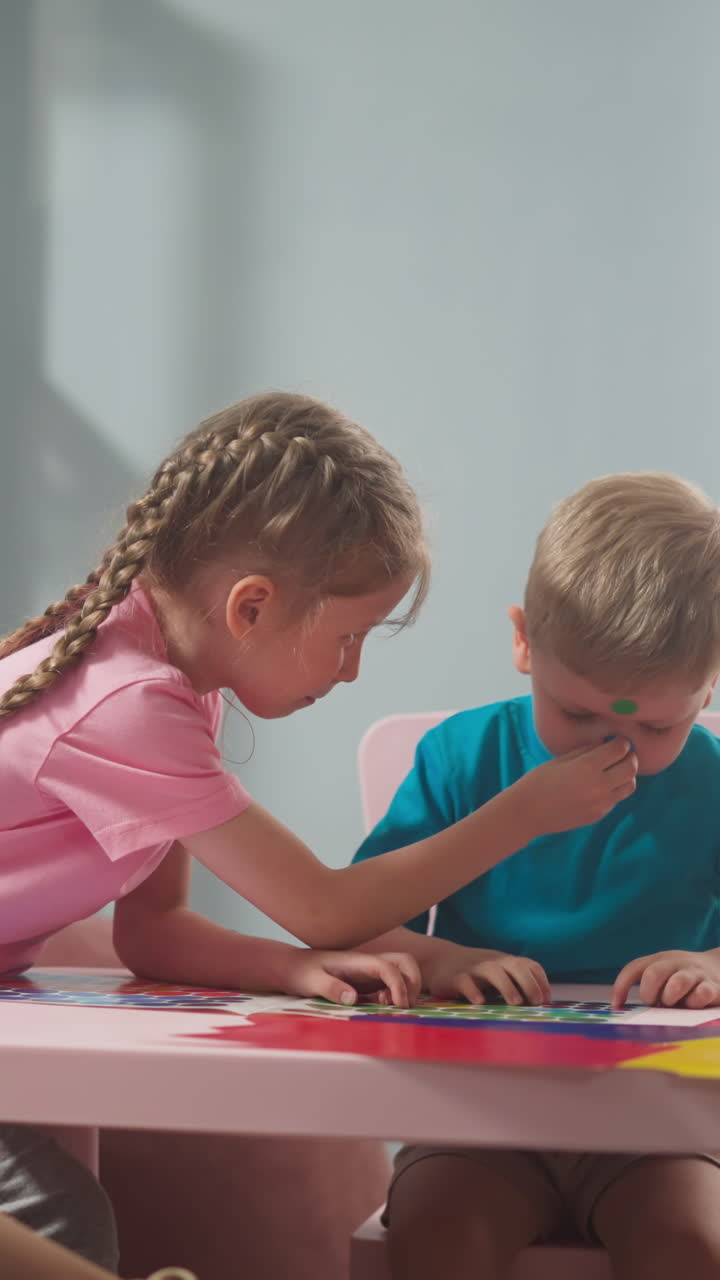 joyful children play with stickers, stick stickers on top of each other, mom is working next to them in room