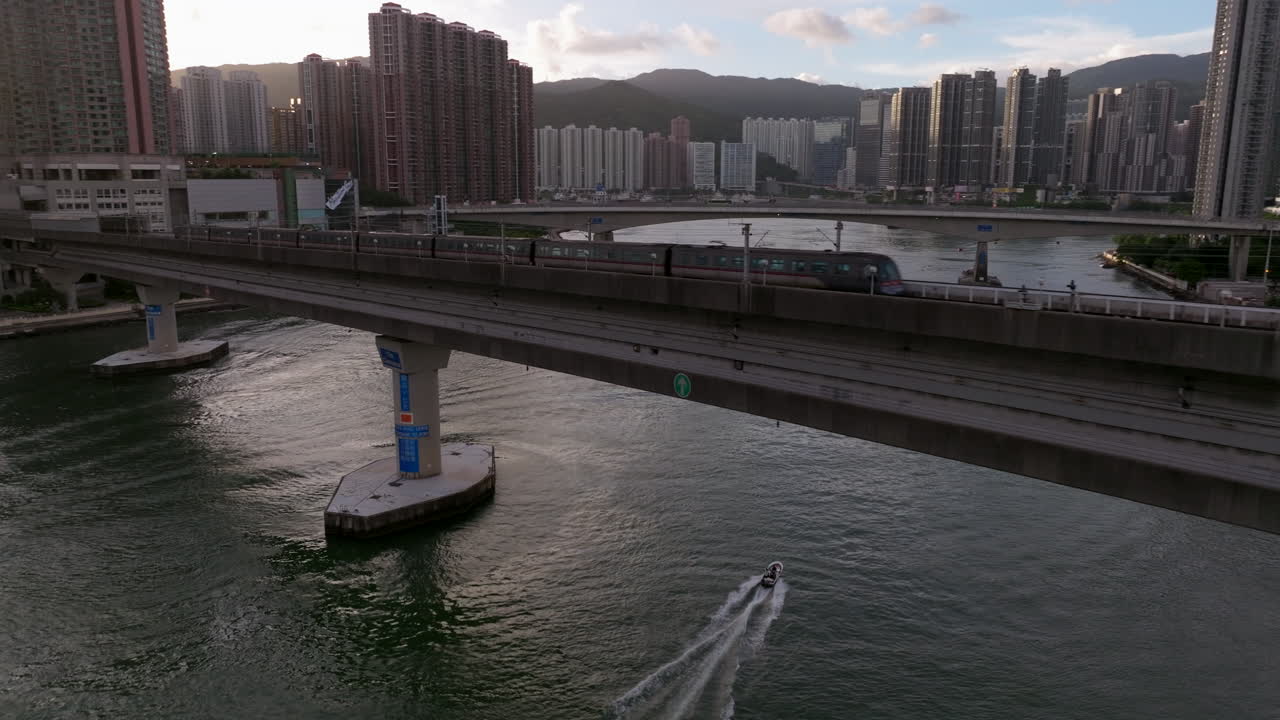 toma aérea hacia atrás en movimiento rápido del tren mtr en el puente hacia la estación tsing yi al atardecer