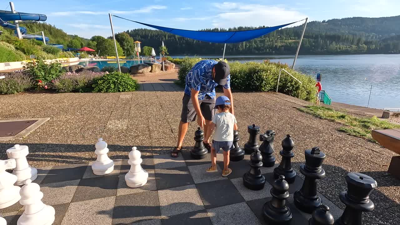 Father and Son Playing Giant Outdoor Chess by a Scenic Lake