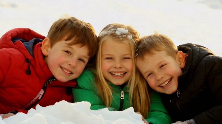 Tre bambini felici che ridono sdraiati nella neve bianca fresca