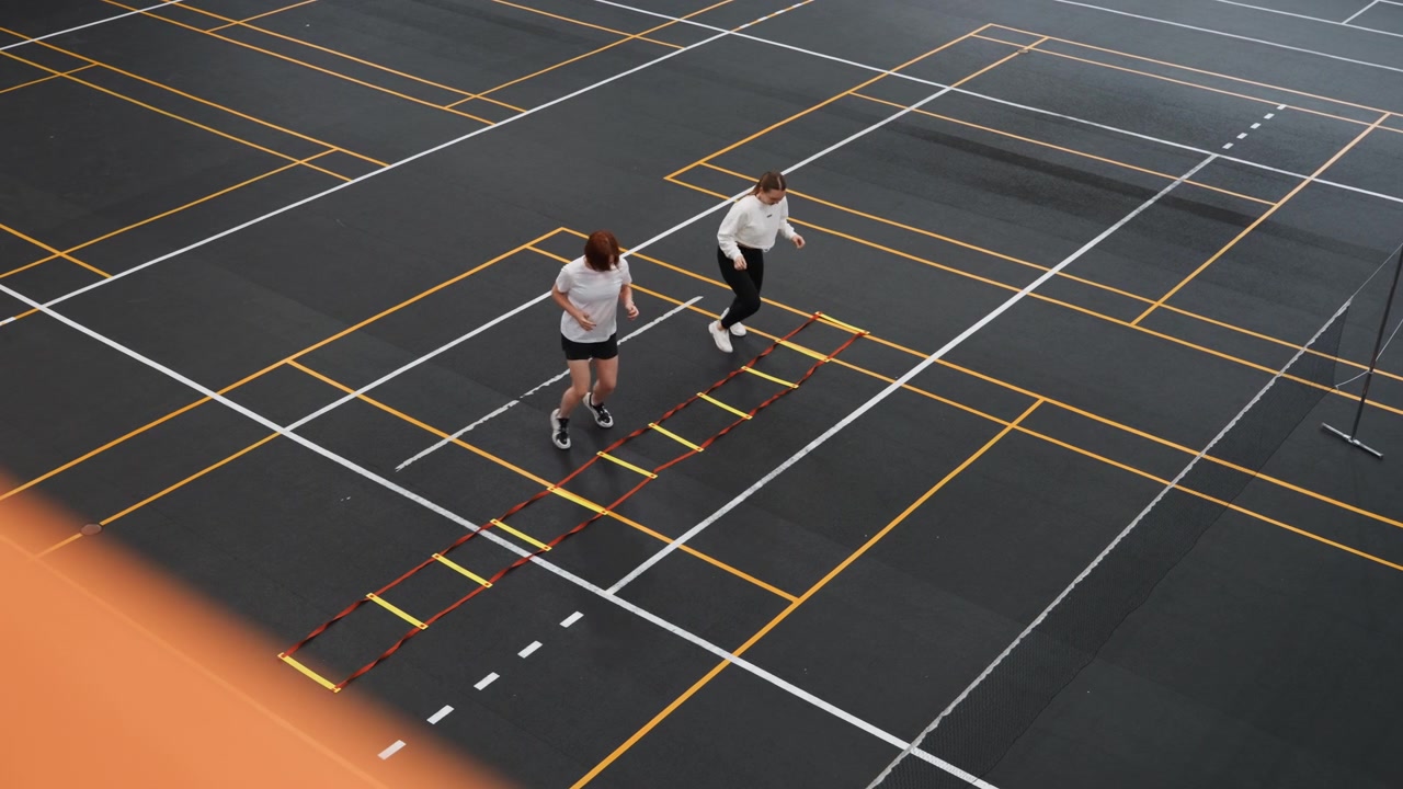 White teammates warming up on badminton court with ladder drill before match, club training environment with upbeat energy and focused drills, players practice timing rhythm and coordination