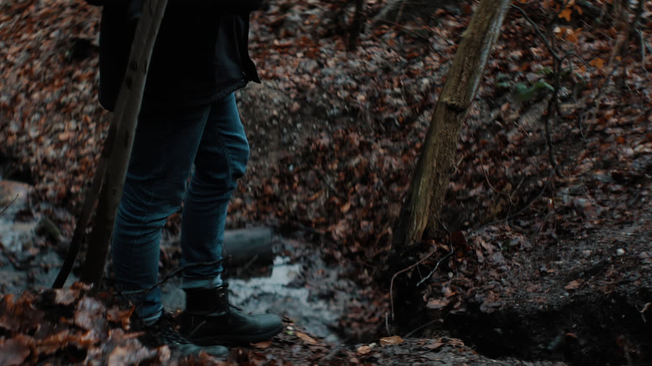 man in boots crossing little stream on a dark autumn day. creek, brook, rivulet in 4K Sow Motion. fall landscape.