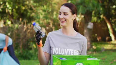 mujer caucásica sonriente con camiseta de voluntario sosteniendo una caja de reciclaje, recolectando residuos plásticos