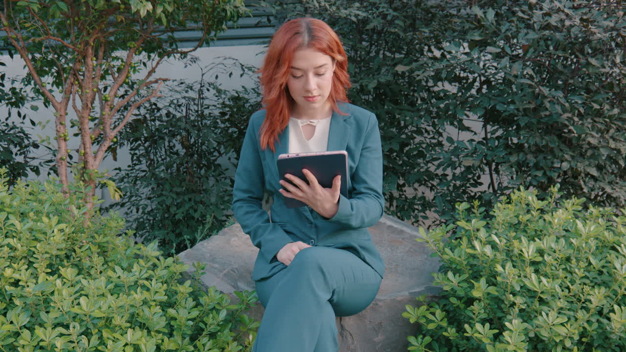 снимок красивой белой женщины, прокручивающей приложения, сидя на скале в парке в ветреный день