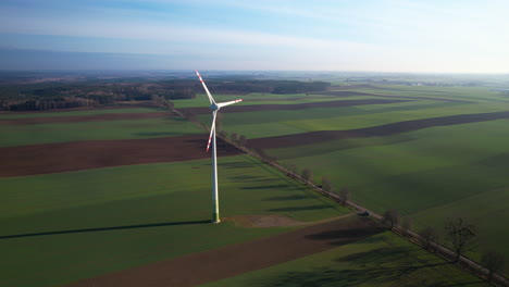 flying toward spinning wind turbine towering by countryside road against plain agricultural farmland in poland - aerial flyover