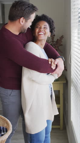 video vertical de una pareja feliz y diversa de pie en la ventana y abrazándose