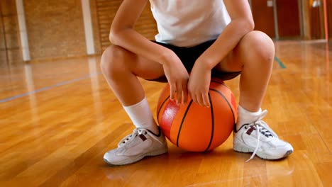 Athletic-African-American-schoolboy-sitting-on-basketball-in-basketball-court-at-school-4k