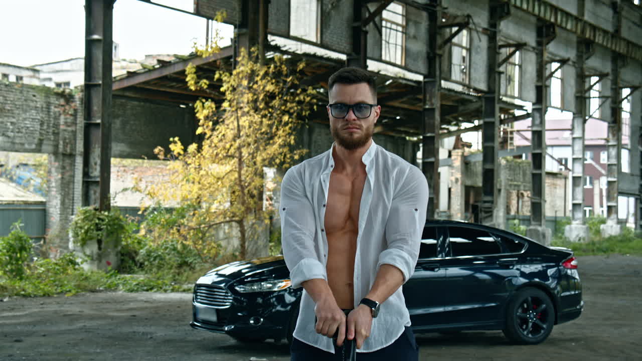 Businessman with a handgun. Young handsome man in shirt and glasses holds pistol in his hand. Serious man with sportive body with a weapon outdoors.